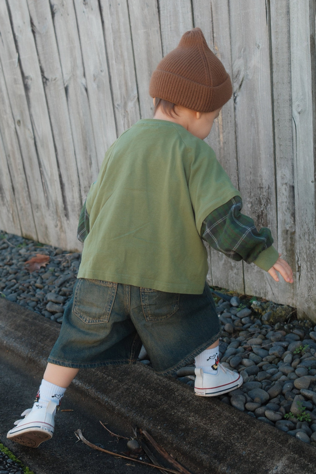 Toddler stepping on curb wearing green cotton plaid lomgsleeve