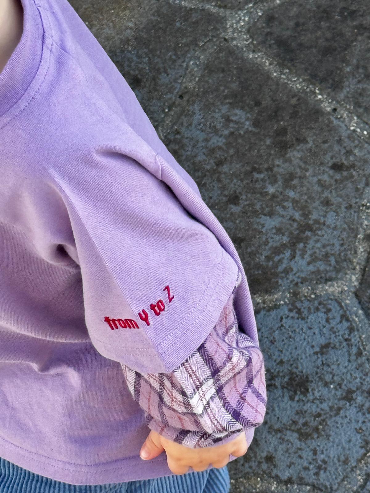 Close-up of a child's arm wearing a purple sleeve with plaid cuffs against a stone pavement background.