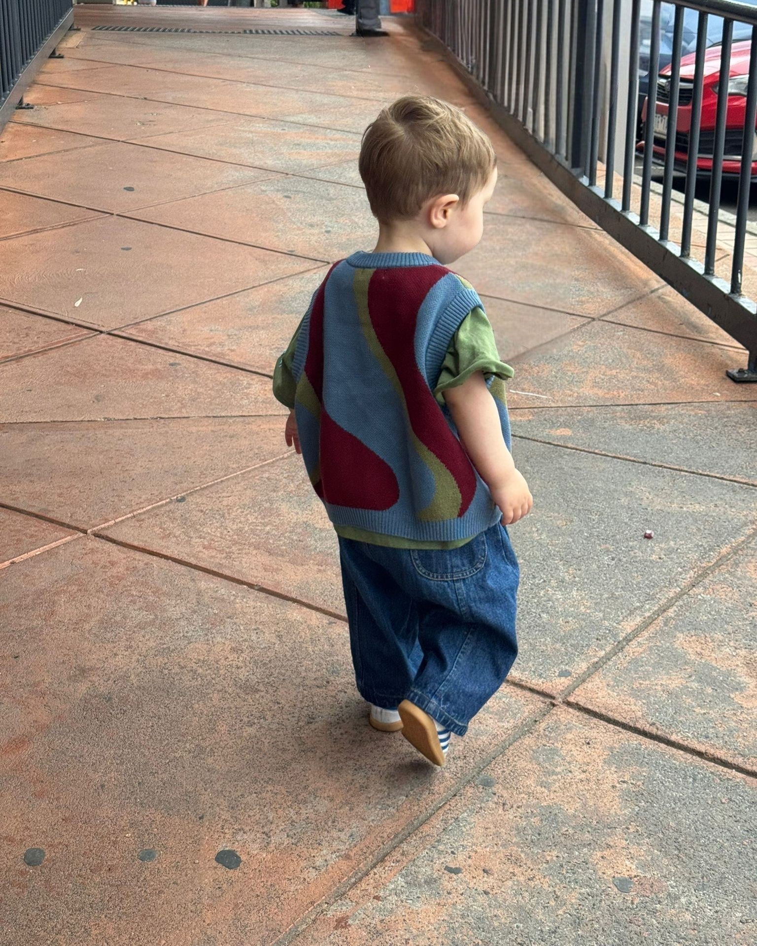 Child wearing a colorful sweater walking on a sidewalk