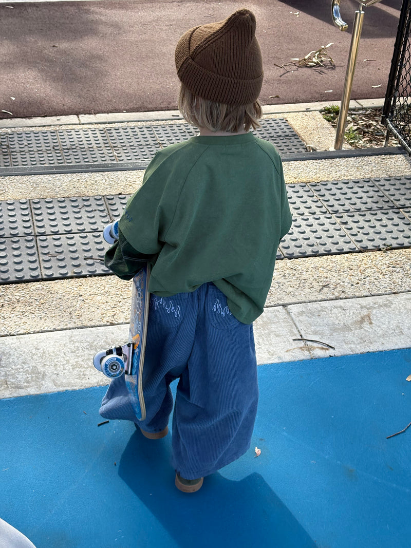 Child wearing ollie double-sleeve in hunter and blaze cord pants in blue flame holding a skateboard