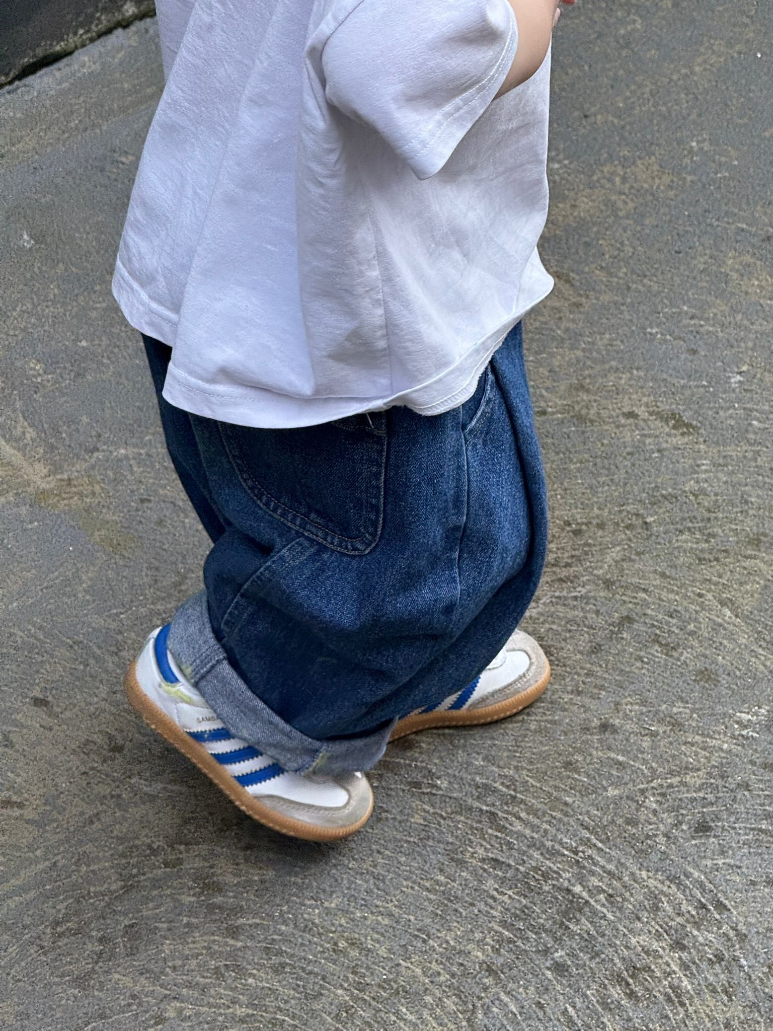 Child wearing blue jeans and white shoes with a focus on the legs and feet.