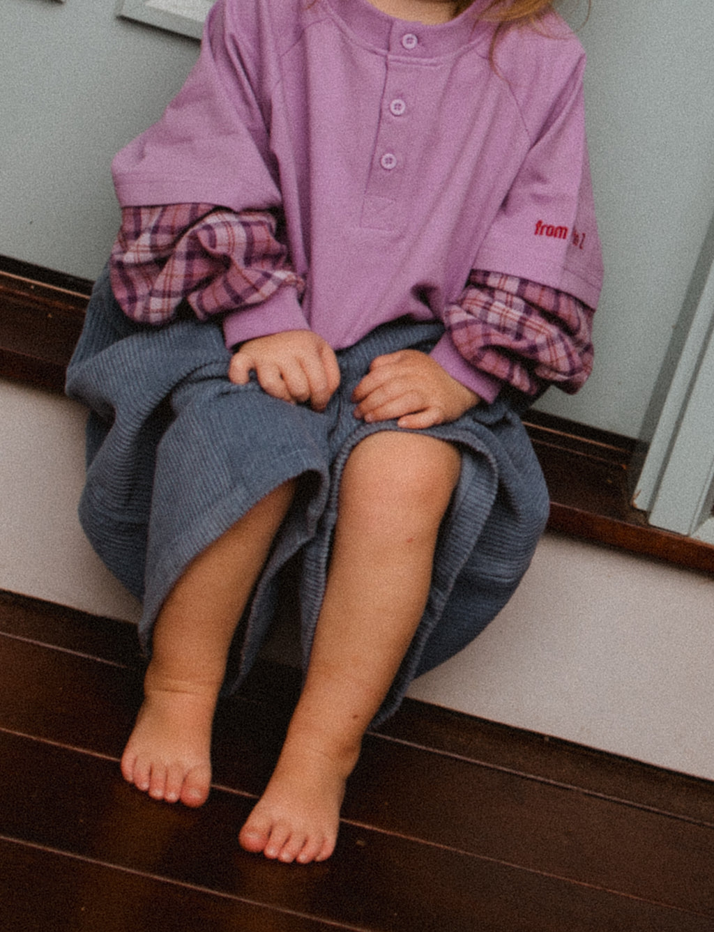 Toddler sitting down wearing purple plaid long sleeve tee ollie double-sleeve in fig