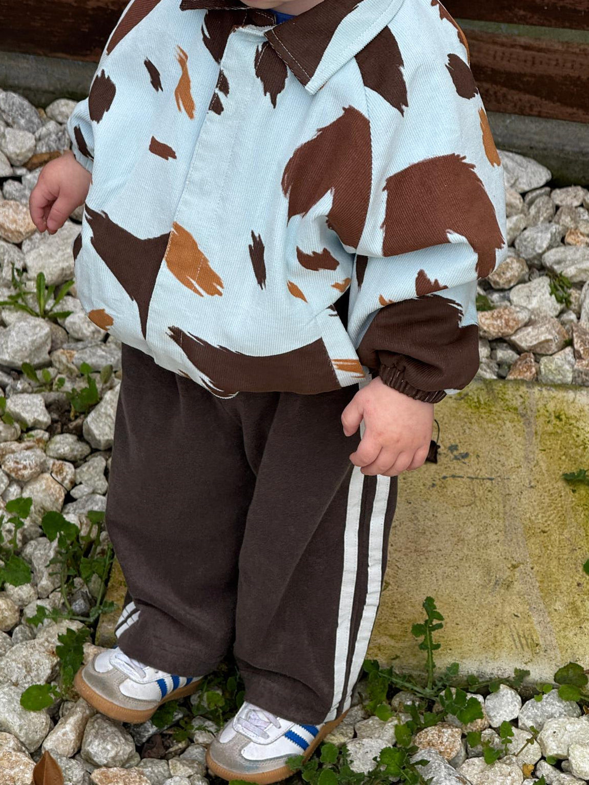 Child wearing a cow print seffi jacket and brown pants standing on rocks.