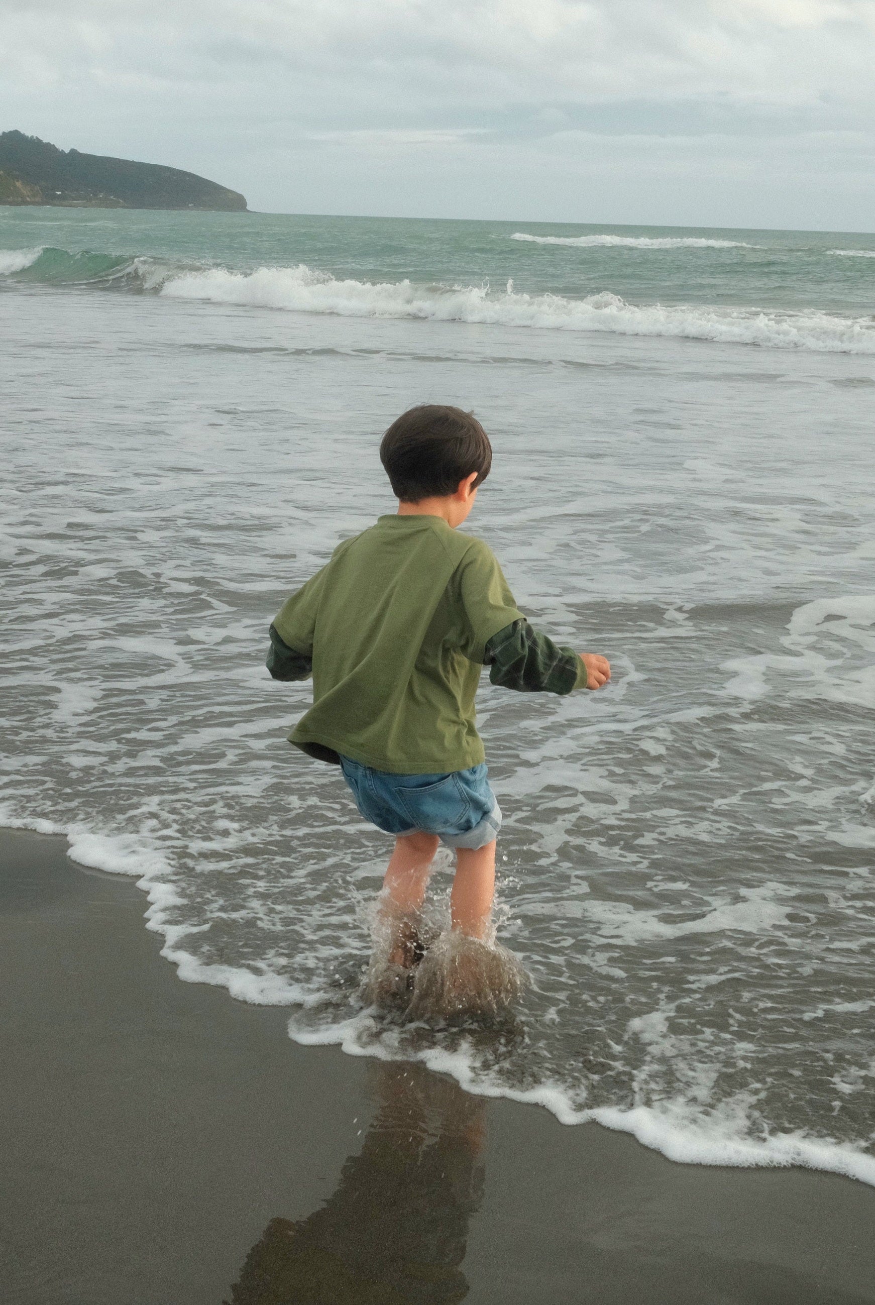 Child at beach wearing ollie double-sleeve in hunter green plaid