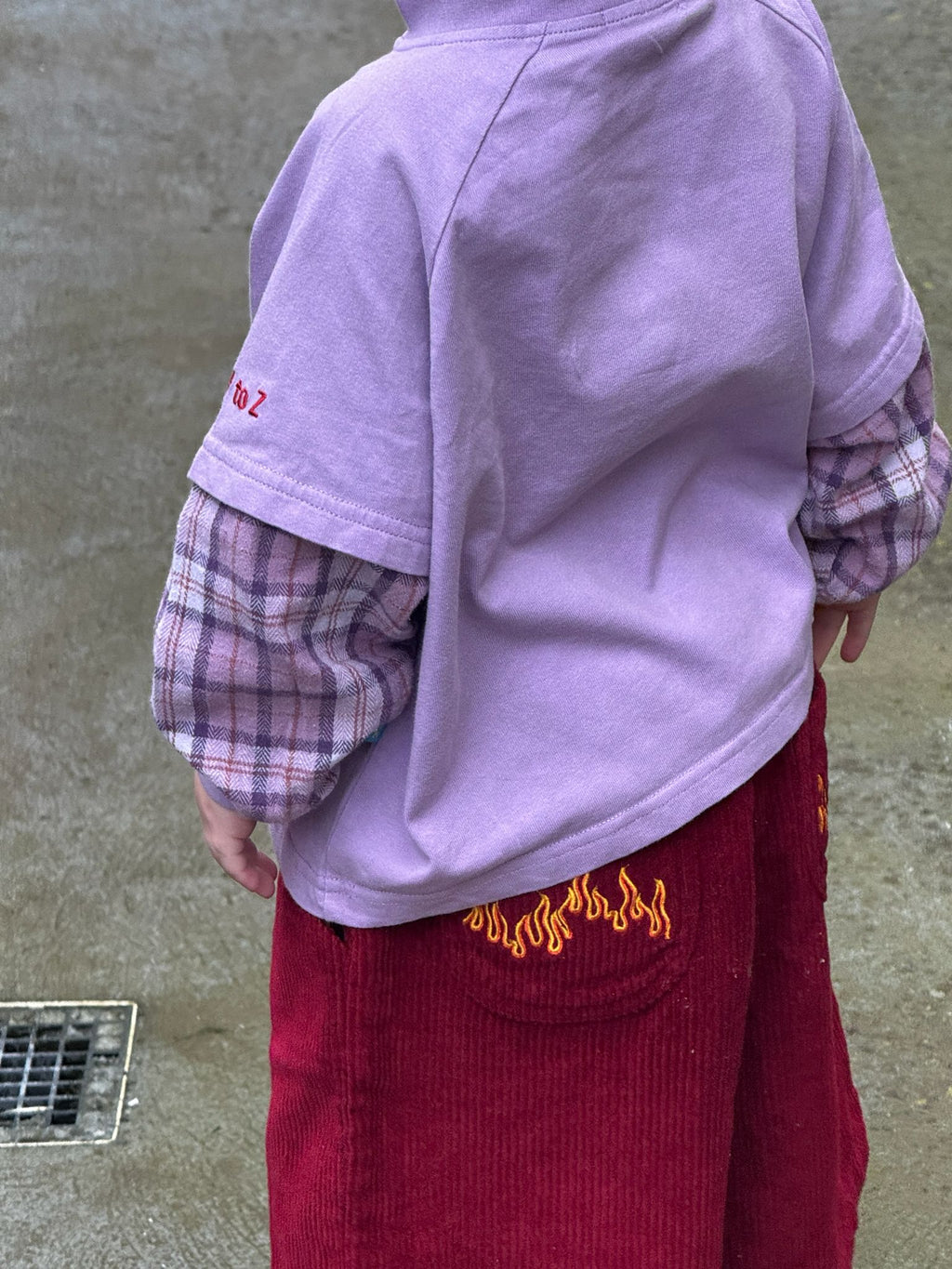 Person wearing a purple plaid longsleeve and red pants with flame design on a concrete floor.